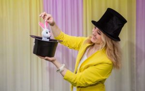 Female magician in yellow jacket pulling a rabbit from a top hat | Start a magician side hustle